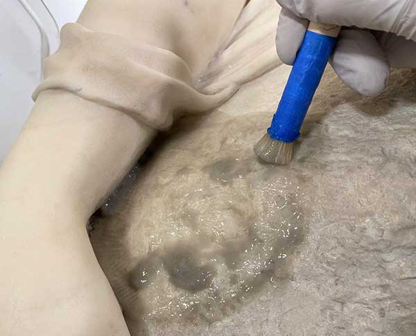 A close-up image of the sculpture surface being cleaned