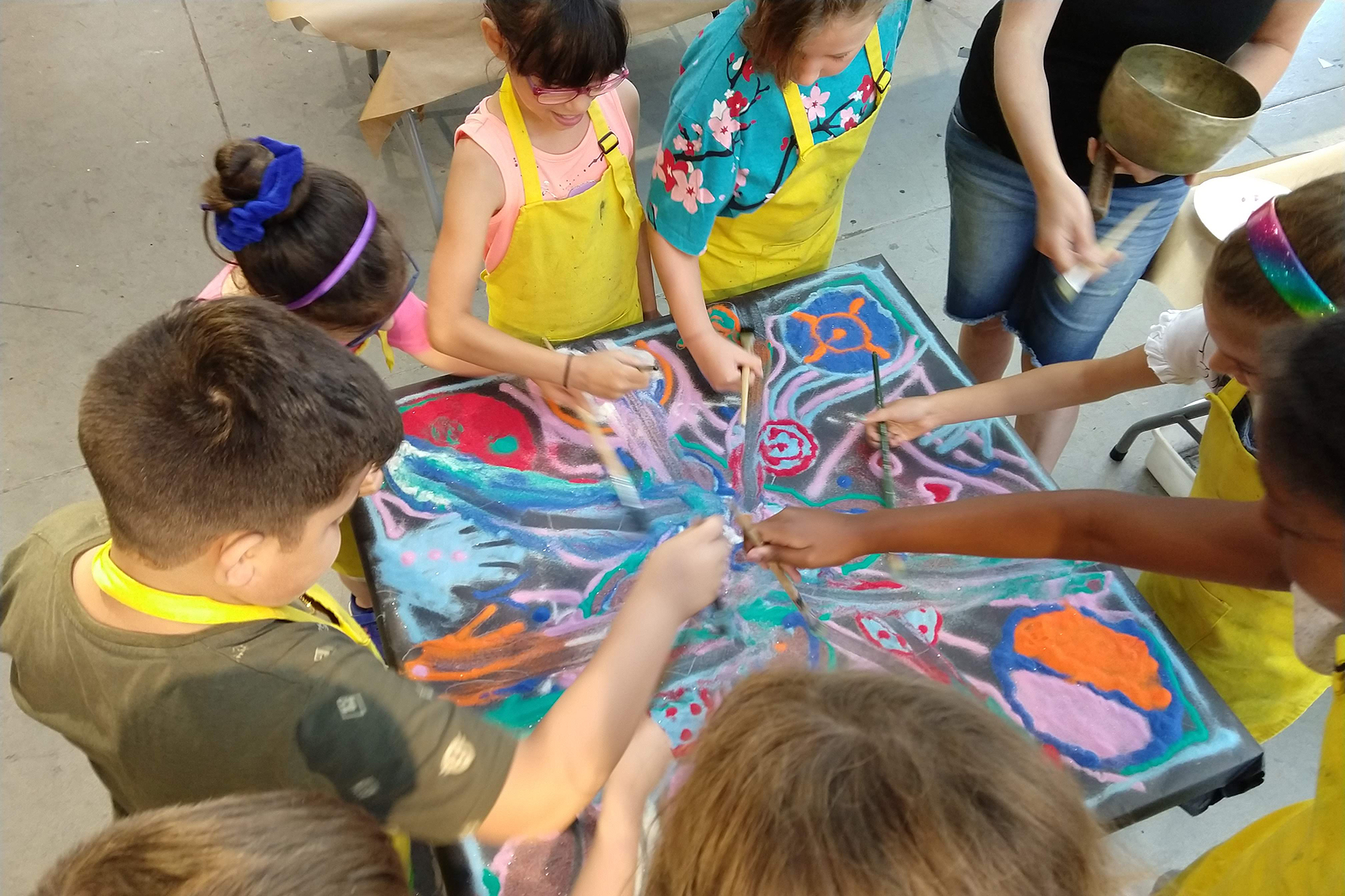 A group of children in yellow aprons gathered around a canvas painting together