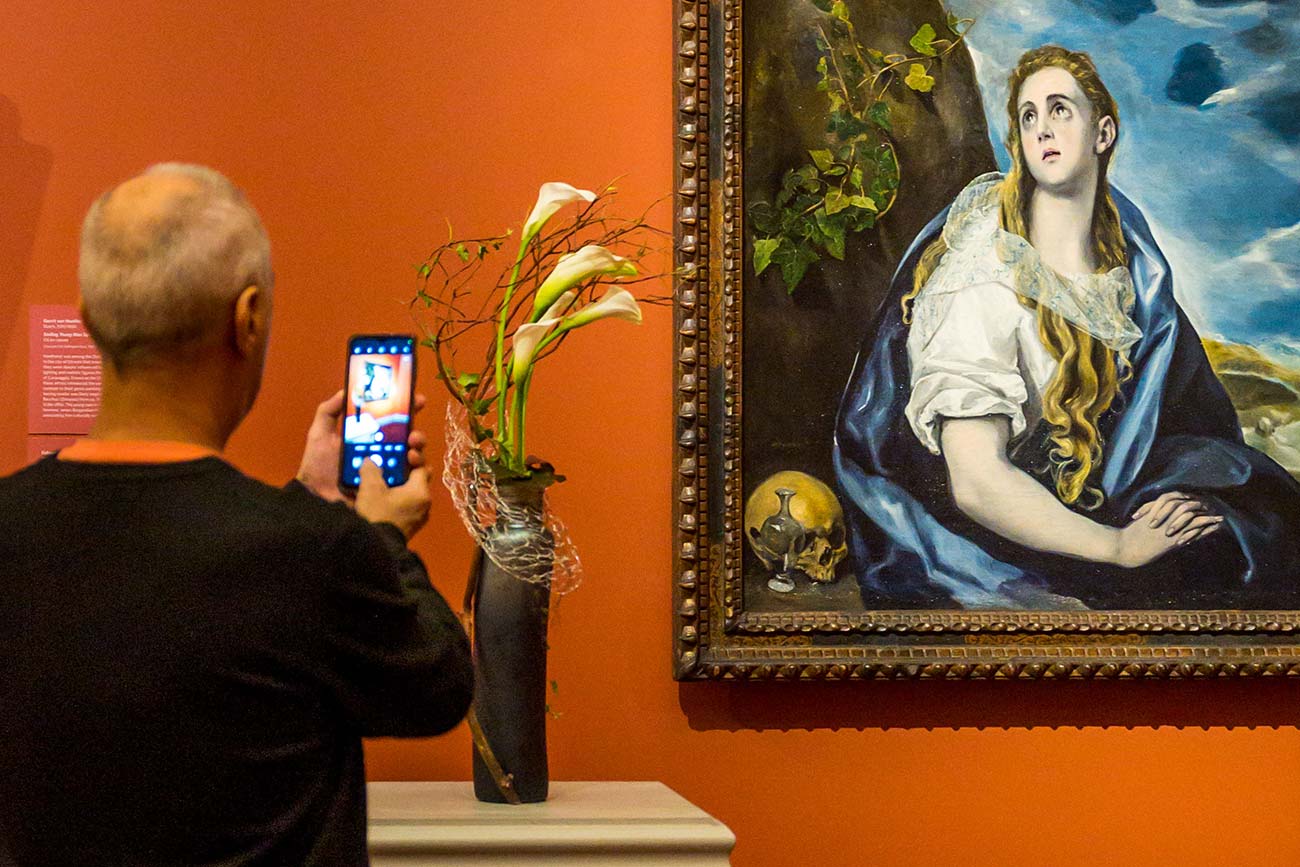 A visitor holds their phone up to take a photo of a floral interpretation