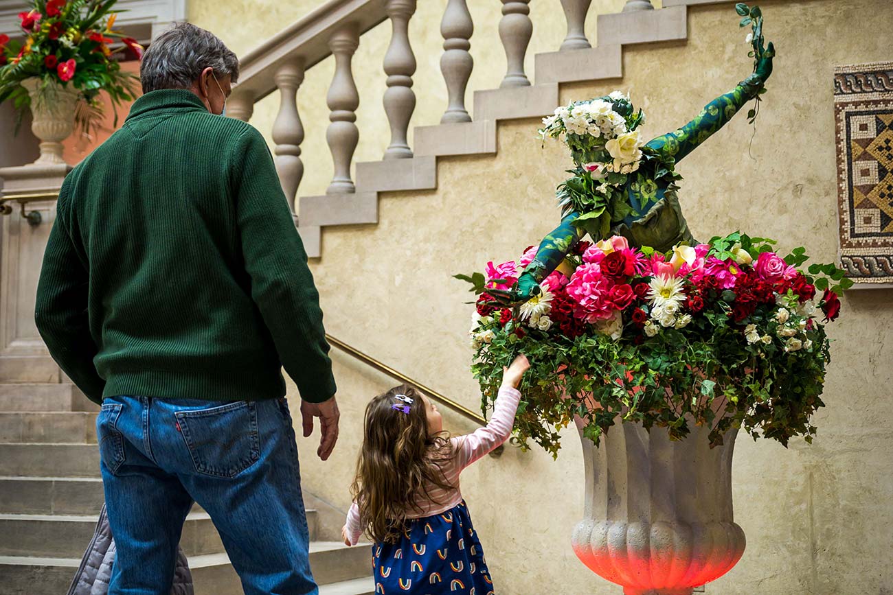 A young child reaches up to shake hands with a 'Living Sculpture' performer