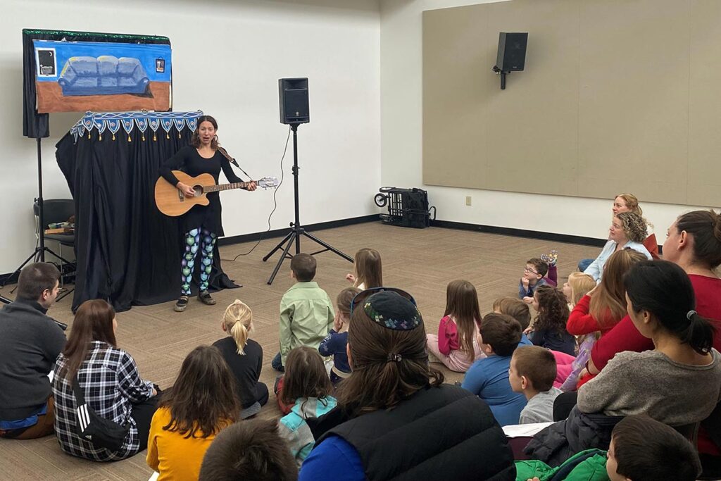 Anna Sobel singing and playing guitar in front of a young audience